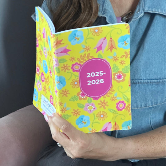 Person holding a colorful planner with floral design and '2025-2026' text.