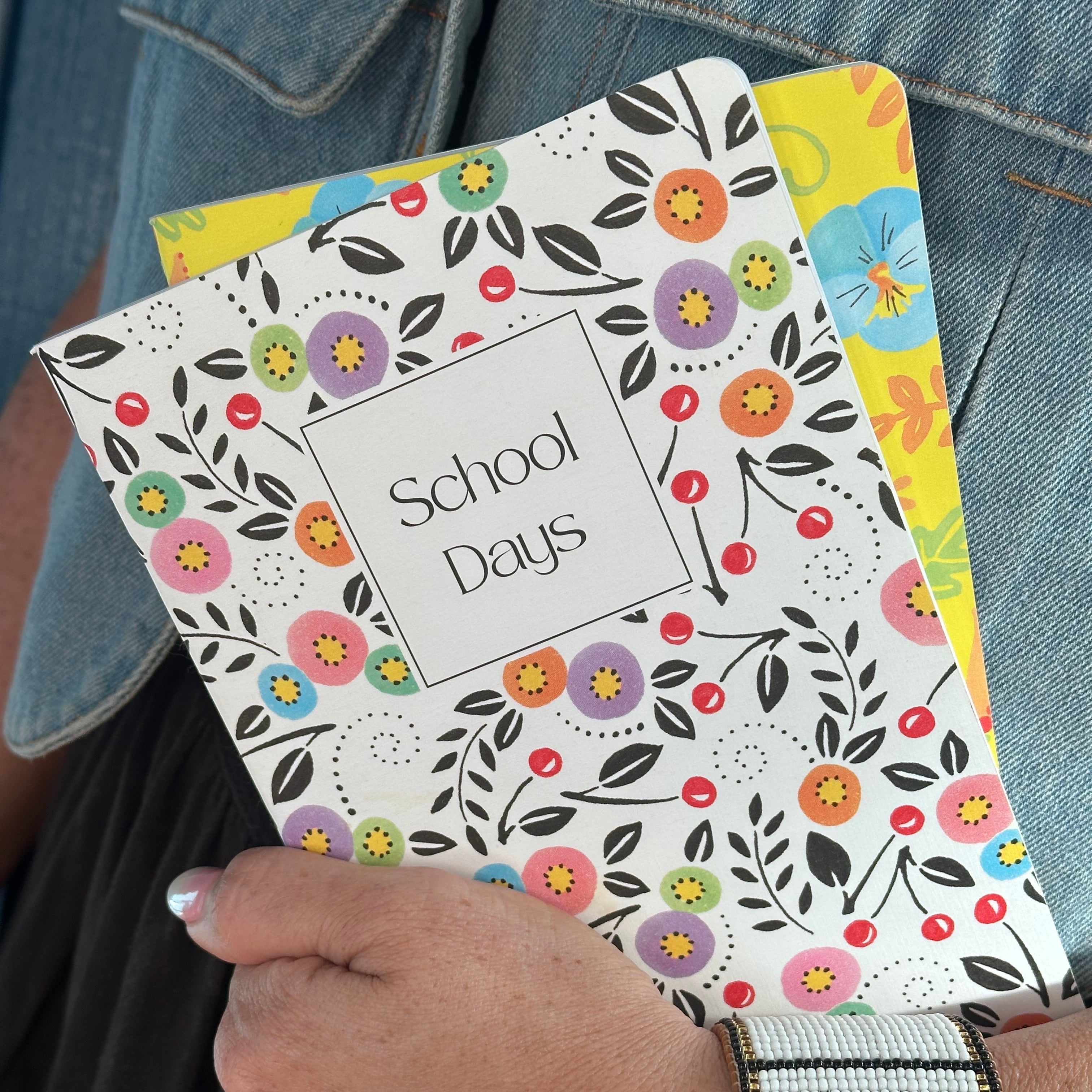Hand holding a floral notebook with 'School Days' text against a denim background